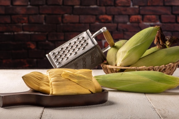Brazylijska przekąska kukurydziana pamonha i zielona kukurydza ułożone na białym rustykalnym drewnianym stole selektywne focus