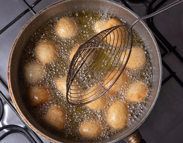 Brazylijski cukierek bolinho de Chuva, wyjęty ze smażenia na patelni z oliwą, widok z góry.