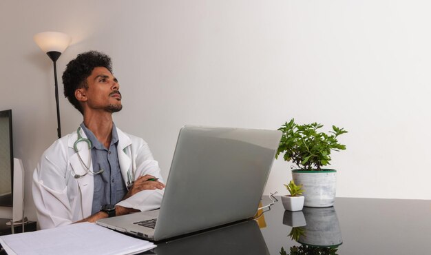 Brazylijski czarny lekarz lub lekarz weterynarii pracujący w domu Młody człowiek robi domowe biuro w ciągu dnia przy biurku z laptopem