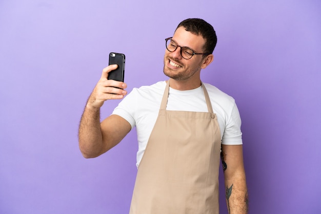 Brazylijski kelner w restauracji na odosobnionym fioletowym tle robi selfie