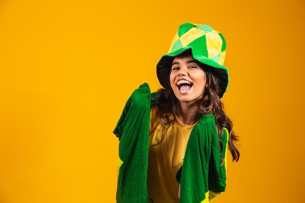 Brazylijski kibic. Brazylijska kobieta fan świętuje na mecz piłki nożnej lub piłki nożnej na żółtym tle. Kolory Brazylii.