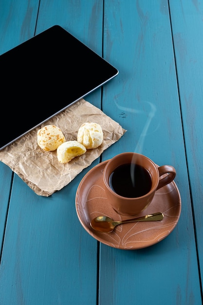 Brazylijskie pieczywo serowe obok filiżanki złotej łyżki i tabletki w pionie