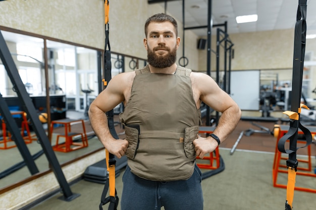 Brodaty dorosły mężczyzna w siłowni, ubrany w kuloodporną kamizelkę pancerną, sport wojskowy