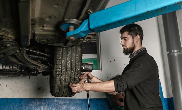 Brodaty mechanik z śrubokrętem naprawiający koło samochodowe w warsztacie