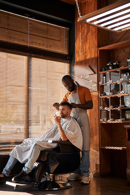 Brodaty męski fryzjer strzyżący włosy klienta nożyczkami