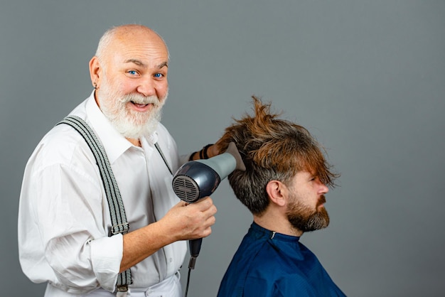 Brodaty mężczyzna coraz fryzurę przez fryzjera z suszarką do włosów u fryzjera. Fryzjer zabawny trzymając suszarkę.