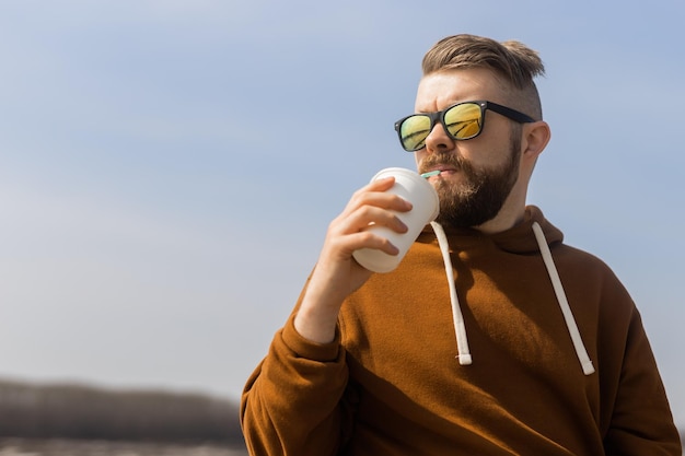 Brodaty mężczyzna pijący szejka na wiosennym deptaku, napoje zabierają i gen z lub milenijną młodość