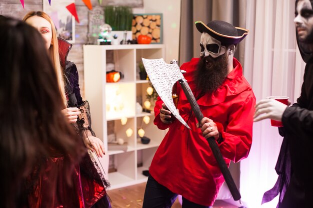 Zdjęcie brodaty mężczyzna przebrany za pirata trzymającego siekierę podczas obchodów halloween ze swoimi potwornymi przyjaciółmi.