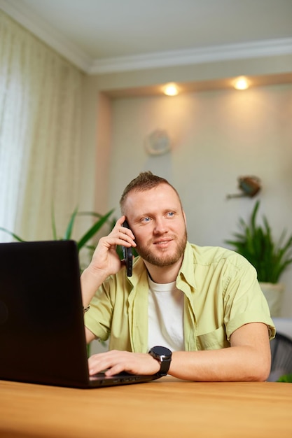 Brodaty mężczyzna rozmawiający przez telefon za pomocą laptopa