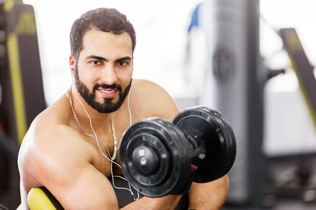 Brodaty mężczyzna topless nosi czarne sportowe rękawiczki ćwiczy biceps na siłowni