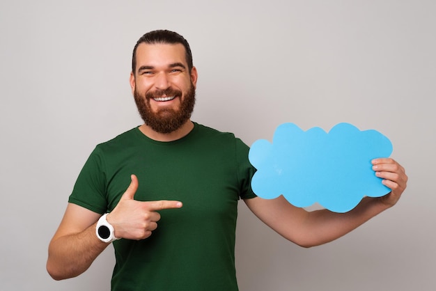 Brodaty mężczyzna trzyma mowę bąbelkową w kształcie niebieskiej chmury i wskazuje na nią