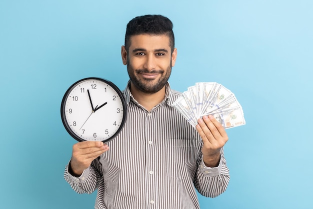 Brodaty mężczyzna trzymający wielkiego fana banknotów dolarowych i zegara ściennego to pieniądze wyrażające szczęście