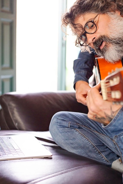 Brodaty mężczyzna uczy się grać na gitarze akustycznej online