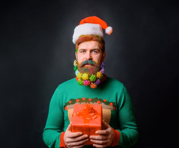 Brodaty mężczyzna w czapce Mikołaja ze zdobioną brodą z prezentem świątecznym Święta noworoczne Wesołych Świąt