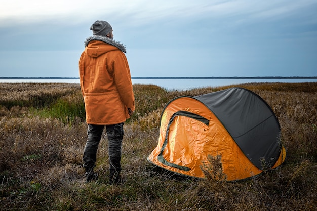 Brodaty Mężczyzna W Pobliżu Namiotu Kempingowego W Pomarańczowej Naturze I Jeziorze. Podróże, Turystyka, Camping.