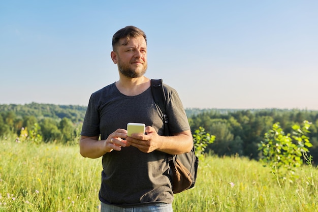 Brodaty mężczyzna w średnim wieku z plecakiem za pomocą smartfona