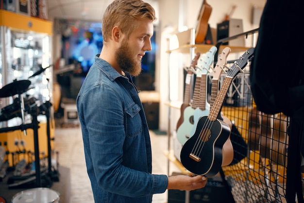 Zdjęcie brodaty młody mężczyzna wybiera gitarę ukulele w sklepie muzycznym. asortyment w sklepie z instrumentami muzycznymi