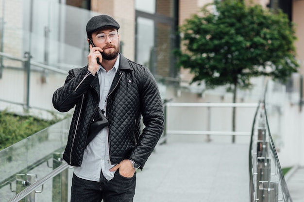 Brodaty, poważny, stylowy menedżer rozmawiający przez telefon na ulicach miasta w pobliżu nowoczesnego biura