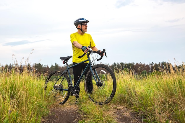 Brodaty rowerzysta w żółtych ubraniach odpoczywa na rowerze na drodze w przyrodzie, hobby sportowym i rozrywce dla zdrowia