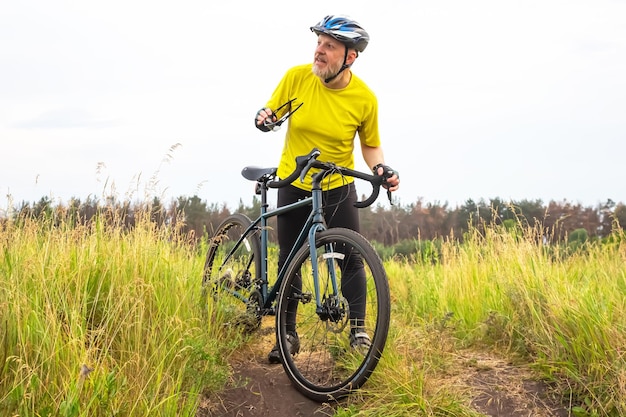 Brodaty rowerzysta w żółtych ubraniach odpoczywa na rowerze na drodze w przyrodzie sporty hobby i rozrywka dla zdrowia