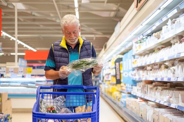 Brodaty starszy mężczyzna pcha wózek na zakupy w supermarkecie, robiąc zakupy spożywcze