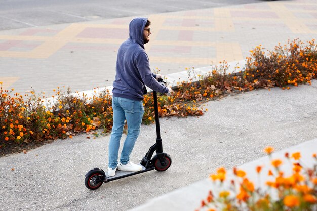 Brodaty stylowy mężczyzna jeżdżący na skuterze elektrycznym Facet na codziennych dojazdach do jazdy na mikroskuterze