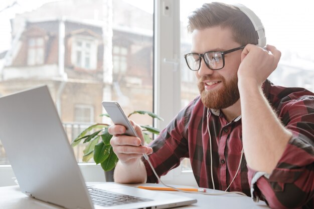 Brodaty Szczęśliwy Młody Człowiek Używa Telefon I Słuchającą Muzykę.