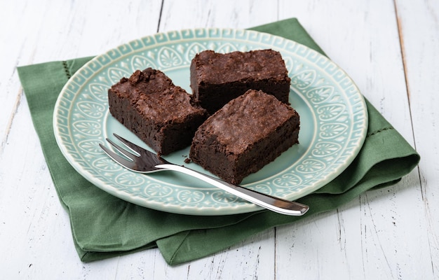 Brownies na zielonym talerzu nad białym drewnianym stołem