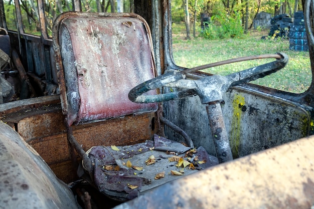 Brudny Stary Fotel Kierowcy Z żółtymi Liśćmi I Kierownicą W Zardzewiałym Autobusie Z Rozbitymi Szybami I śladami Farby W Lesie. Bunkier Na Boisku Do Paintballa Taktycznego. Zamknąć Widok