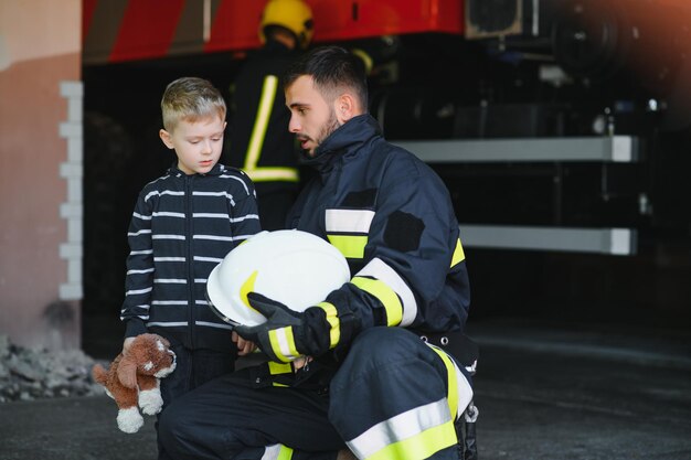 Zdjęcie brudny strażak w mundurze trzymający małego uratowanego chłopca stojącego na czarnym tle