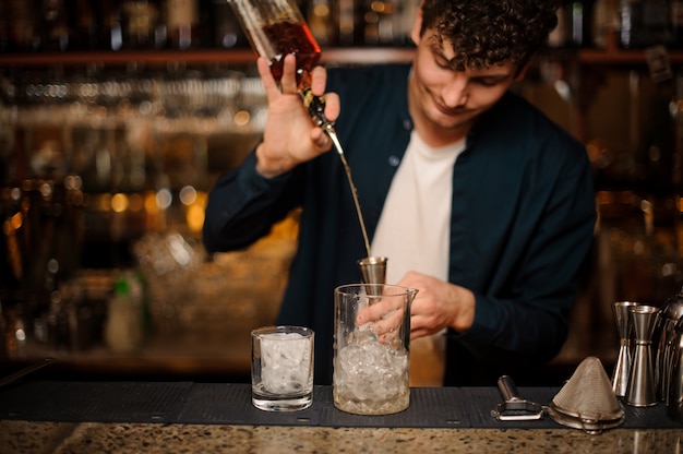 Brunet barman nalewa napój alkoholowy do miarki