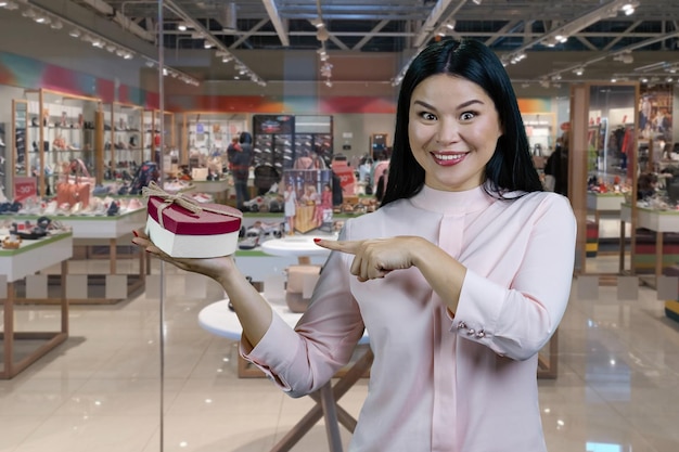 Brunetka azjatycka kobieta wskazująca na kształt serca pudełko butikowe wnętrze butiku w tle