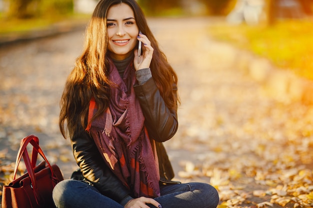 brunetka dziewczyna za pomocą swojego telefonu, jak ona jest relaks w parku podczas jesieni