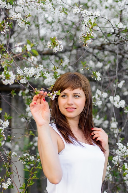 Brunetka dziewczynka w białej sukni na wiosnę na kwiat wiśni