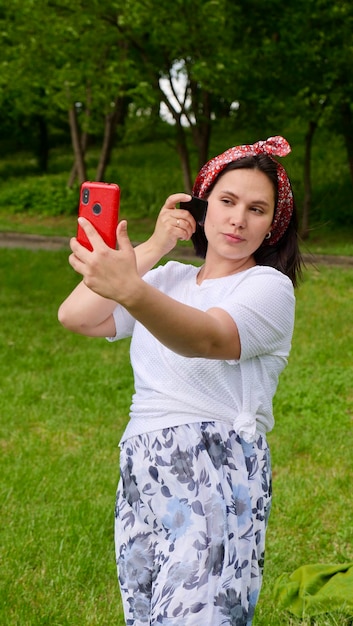 Brunetka kaukaska kobieta z jadeitową skrobaczką gwaszową na zewnątrz dziewczyna robi gwaszowy masaż twarzy przed telefonem Pojęcie piękna i samoopieki pielęgnacja skóry i twarzy Pionowe zdjęcie