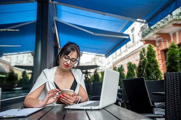 Brunetka kobieta biznesu w stylowym eleganckim garniturze pracująca na laptopie w kawiarni na ulicy