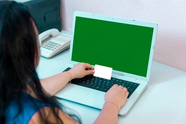 Brunetka kobieta odwrócona plecami do aparatu robi zakupy w Internecie, płacąc kartą bankową online green screen. Zdjęcie poziome