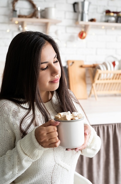 Brunetka kobieta trzyma kubek kakao ptasie mleczko w kuchni