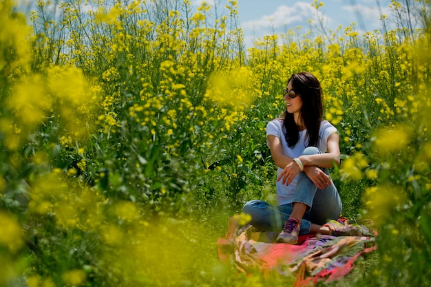 Brunetka kobieta w okularach przeciwsłonecznych w środku kwitnącego pola