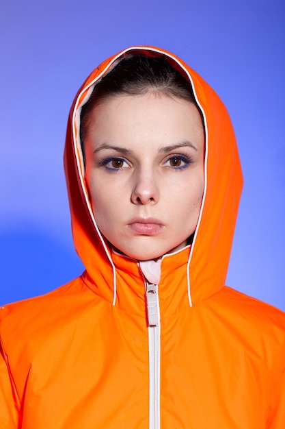 brunetka kobieta w pomarańczowej kurtce na niebieskim tle Wysokiej jakości zdjęcie