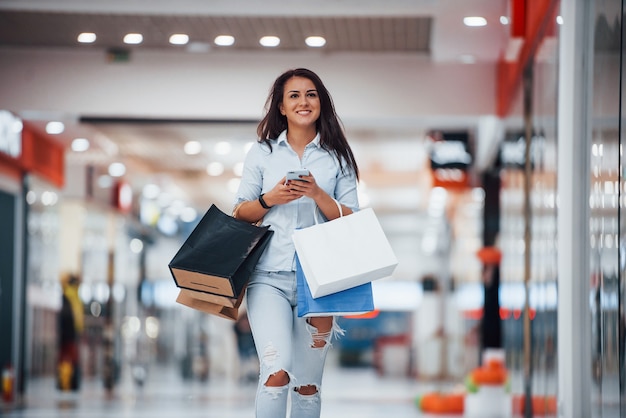 Brunetka kobieta w supermarkecie z wieloma pakietami i telefonem w ręce mają dzień zakupów.