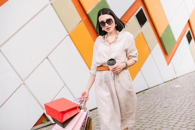 Brunetka kobieta z torbami na zakupy pozuje na kolorowej ścianie sklepu