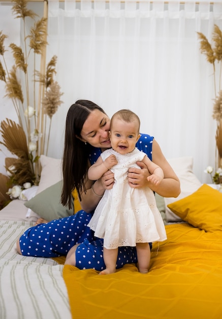 Brunetka Mama Całuje Swoją Córeczkę W Białej Sukience Na łóżku W Sypialni