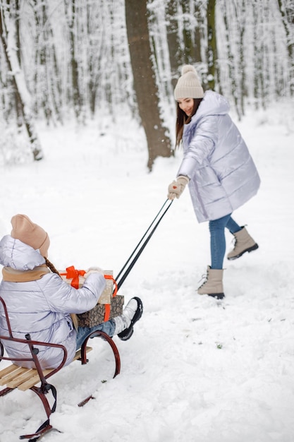 Brunetka mama i jej córka jeżdżą na sankach w zimowym lesie