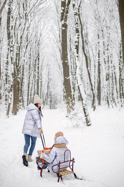 Brunetka mama i jej córka jeżdżą na sankach w zimowym lesie