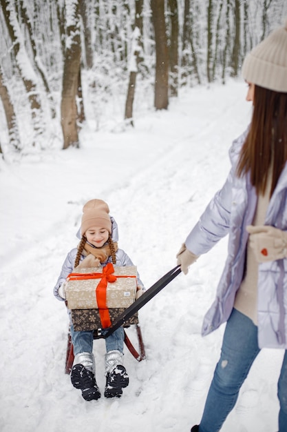 Brunetka mama i jej córka jeżdżą na sankach w zimowym lesie