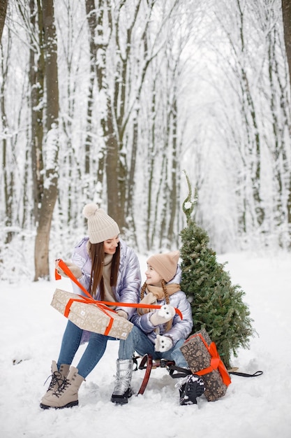 Brunetka mama i jej córka jeżdżą na sankach w zimowym lesie