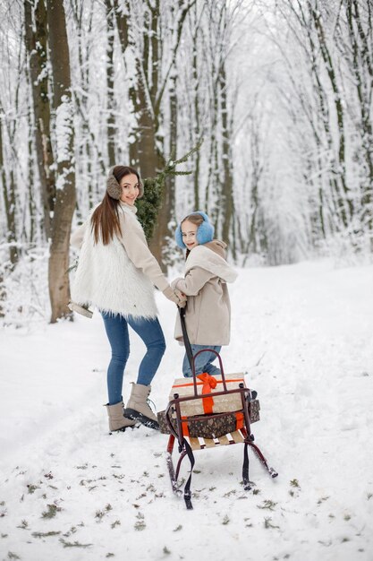 Brunetka matka i jej córka stoją w pobliżu sań w zimowym lesie