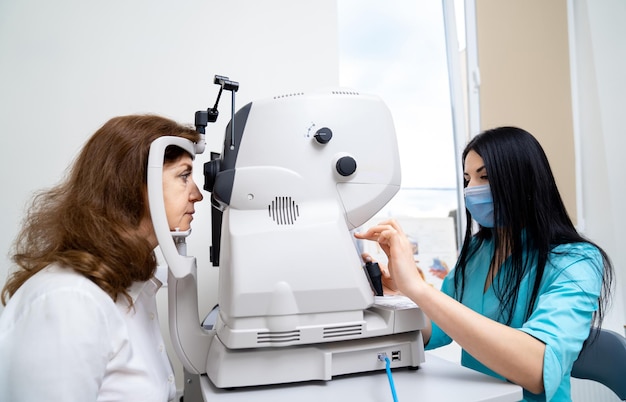 Brunetka optometrystka diagnozuje kobietę na specjalnym nowoczesnym sprzęcie Aktualna klinika dla zdrowych oczu Zbliżenie