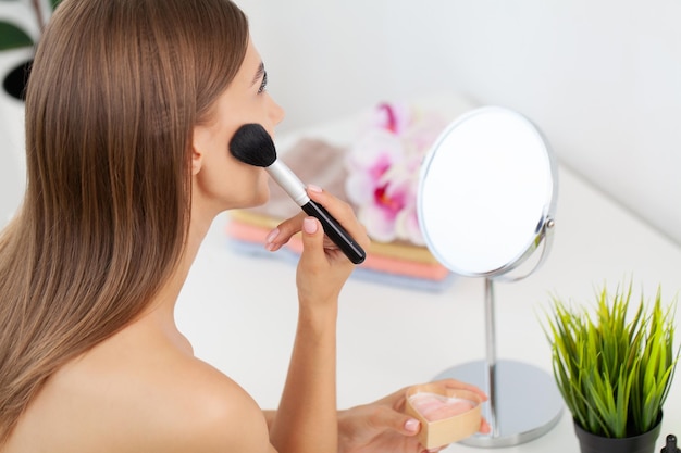 Brunetka piękna kobieta robi makijaż przed lustrem